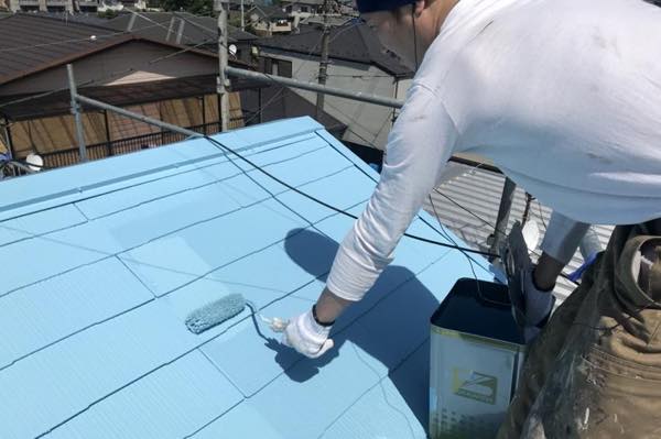 屋根をローラーで青く塗る職人